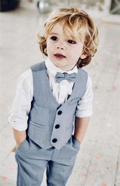 a little boy in a suit and bow tie is standing on the sidewalk with his hands in his pockets