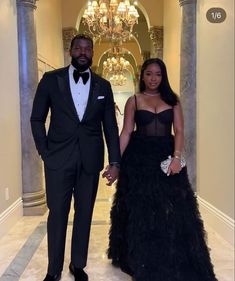 a man in a tuxedo and a woman in a black dress holding hands