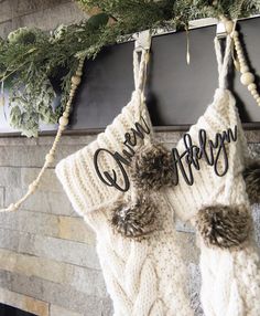 two knitted stockings hanging from a mantel decorated with evergreen needles and holiday decorations