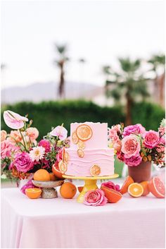 a pink cake sitting on top of a table next to oranges and other fruit