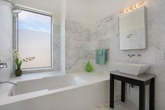 a bathroom with marble walls and flooring, white bathtub next to a large window