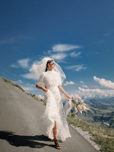 a woman in a wedding dress is walking down the road with her veil blowing in the wind