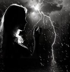 a woman is standing in the rain with her hand up to her face and lightning behind her