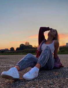 a woman sitting on the ground with her head in her hair and wearing white sneakers