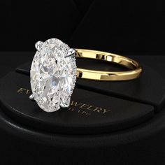 an oval cut diamond ring sitting on top of a black box with gold trimming