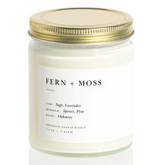 a white candle with a gold lid and label on the top that says fern + moss