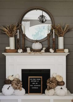 a mantel with pumpkins and candles on it in front of a round mirror