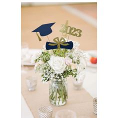 a vase filled with white flowers and topped with two graduation hats sitting on top of a table