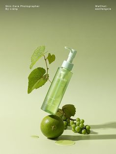 a bottle of green liquid sitting on top of an apple next to grapes and leaves