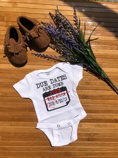 a baby's outfit, shoes and plant on a wooden floor next to a t - shirt that says due dates are four