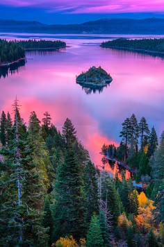 an island in the middle of a lake with trees around it and colorful sky above