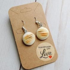 a pair of earrings with white and yellow stripes on them sitting on top of a piece of cardboard