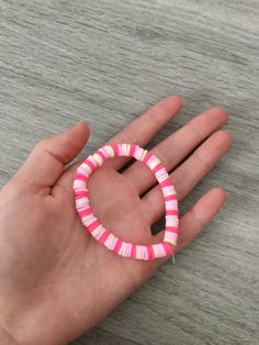 a hand holding a pink and white bracelet on it's palm with two fingers