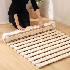 a woman kneeling on the floor next to a bed frame made out of wooden planks