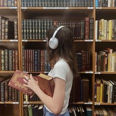 a young woman is listening to headphones while holding a book in front of a bookshelf