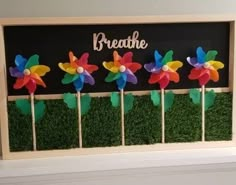 some colorful pinwheels are placed in the grass on top of a blackboard