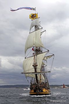 a large white sail boat in the middle of the ocean with flags on it's mast