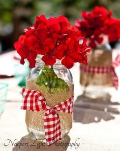 two vases with red flowers in them sitting on a white table cloth covered table