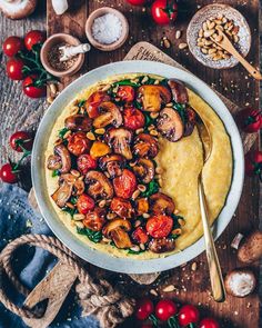 a white bowl filled with food on top of a wooden table next to tomatoes and mushrooms