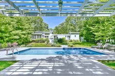 an outdoor swimming pool surrounded by greenery and trees in front of a white house