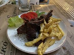 a white plate topped with steak and french fries next to a bowl of salad on top of a table