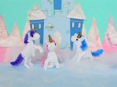 three stuffed unicorns standing in front of a blue and white castle with snow on the ground