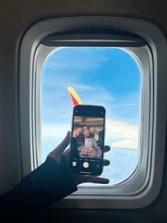 a person taking a photo on their cell phone while flying in the sky with an airplane window