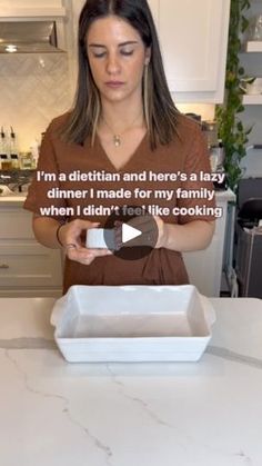 a woman standing in front of a white counter top holding a pan with food inside of it