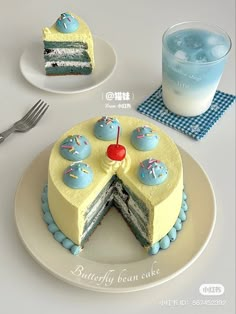 a blue and yellow cake on a white plate next to a glass of ice water