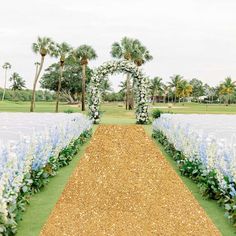 an outdoor ceremony setup with blue and white flowers on the grass, surrounded by palm trees