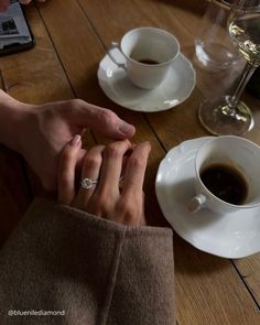 two people holding hands over a cup of coffee and saucer on a wooden table