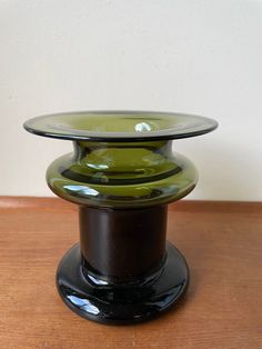 a black and green glass vase sitting on top of a wooden table next to a white wall