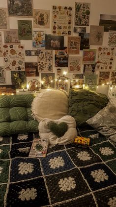 a bed covered in lots of pillows and blankets next to a wall with pictures on it