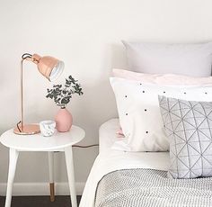 a bed with white sheets, pillows and a pink lamp on the end table in front of it