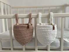 two baskets hanging from the side of a crib in white and beige colors, one with handles