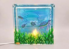 a glass block with sea turtles in the water and grass under it, on a white background