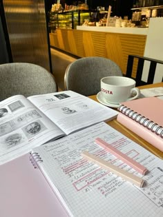 an open notebook sitting on top of a wooden table next to a cup and saucer