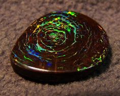 an opalite stone sitting on top of a sandy surface with green and blue colors