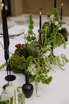 the table is set with black candles and greenery on it, along with other decorations