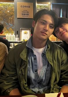 two young men sitting next to each other in front of a table with food on it