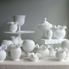 several white vases and bowls sitting on top of a cake platter in front of a gray wall