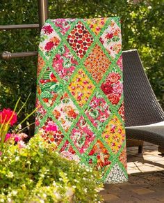 a colorful quilt sitting on top of a chair next to flowers