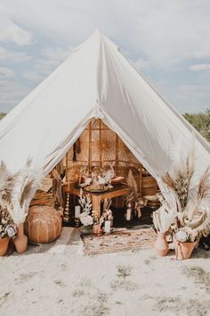 a large white tent sitting on top of a sandy beach next to plants and potted plants