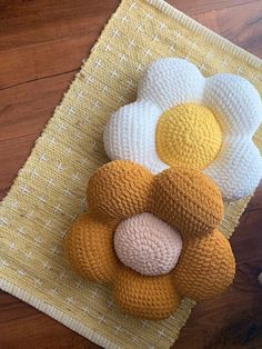 three crocheted flowers sitting on top of a yellow place mat next to each other