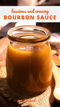 a glass jar filled with bourbon sauce on top of a wooden table next to a spoon