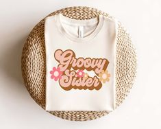 a white t - shirt with the words grooy sister on it sitting on a wicker basket