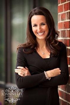 a woman leaning against a brick wall with her arms crossed