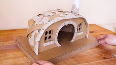 two hands are working on a cardboard house made out of cardboard and paper machs