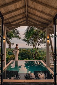 a woman standing on the edge of a pool in front of palm trees and greenery