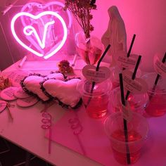 a table topped with lots of cups filled with liquid next to a neon heart sign